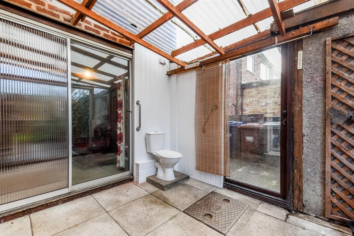 An interior shot of a lean-to, glass-walled extension, with a plumbed in toilet right by the glass wall