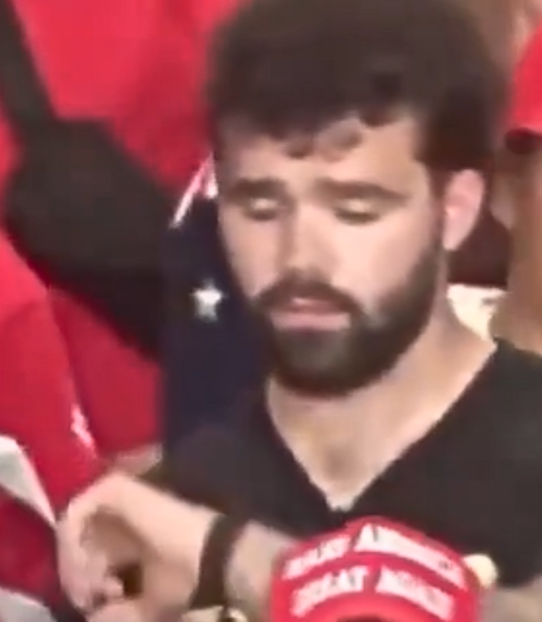 A young bearded man with a pained look on his face, looking at his watch.